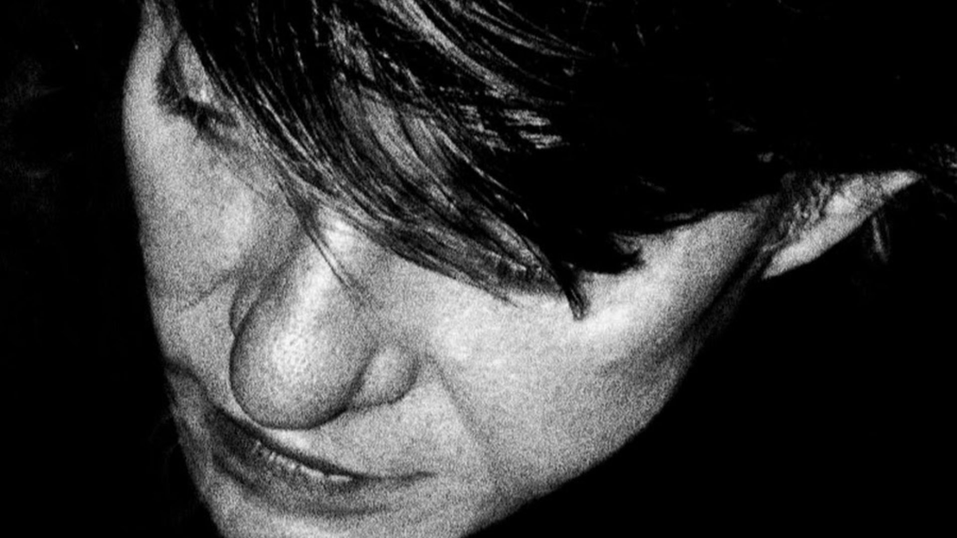 Foto di Fabrizio de André in bianco e nero, con un close-up dall'alto sulla sua faccia, gli occhi coperti dai capelli.